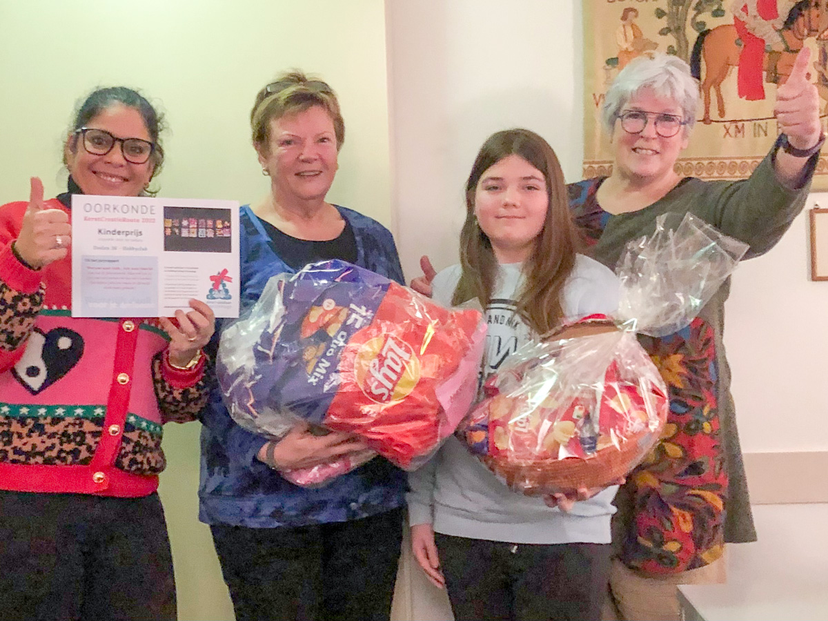 Roxanne Houshmand toont de oorkonde van de Kinderprijs. Ineke Buijnsters en Yfke houden de prijs met chips vast. En annemarie Goosens steekt haar duim op.