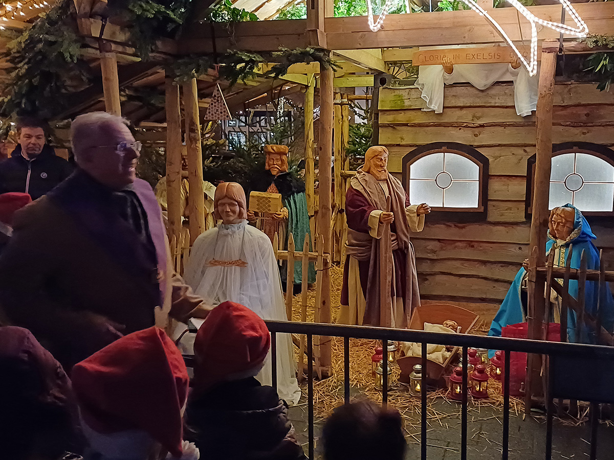 pastor loopt naar de verlichte kerststal met Maria en Jozef