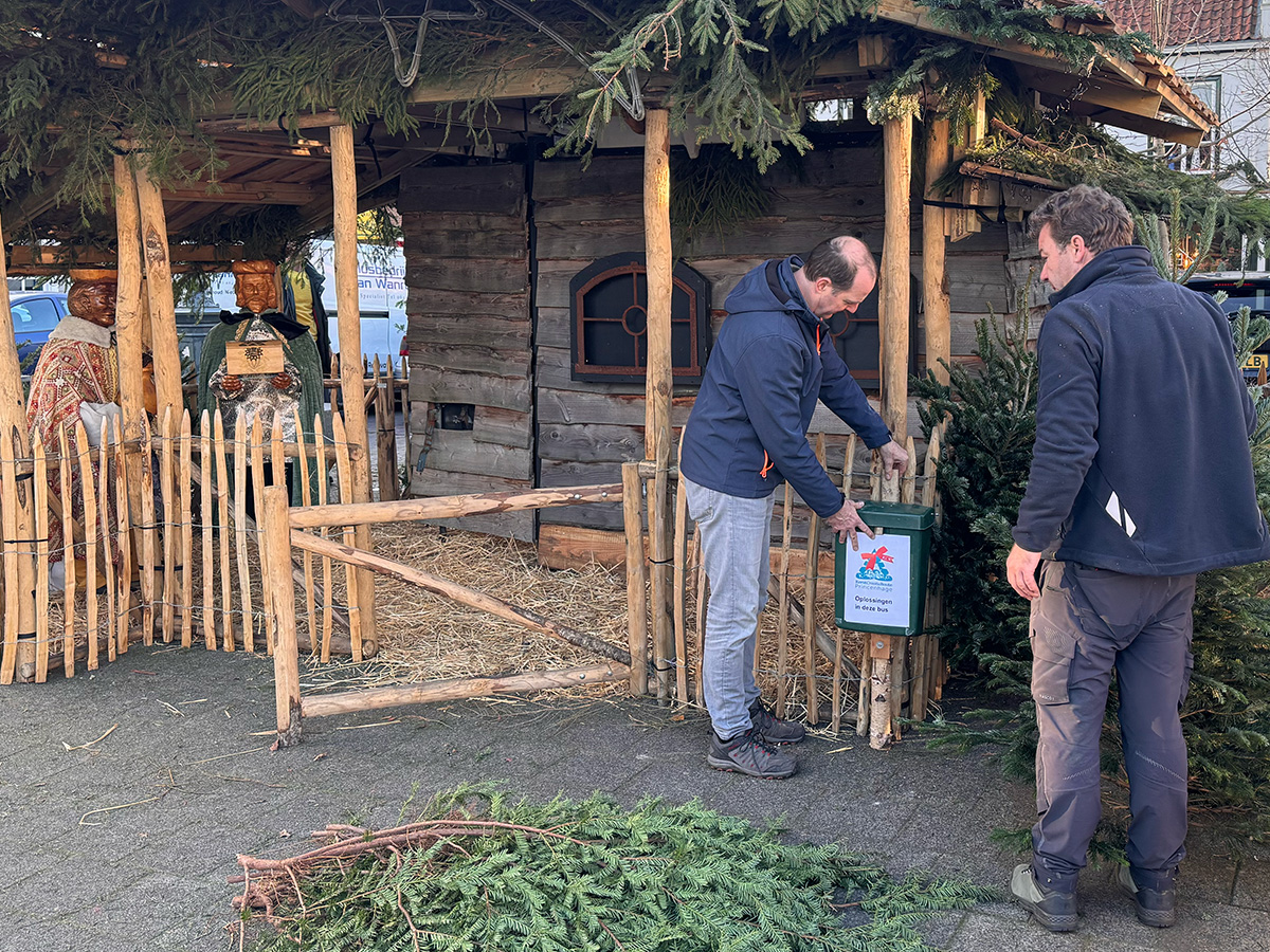 Xander maakt de groene brievenbus vasy aan het hek van de kerststal