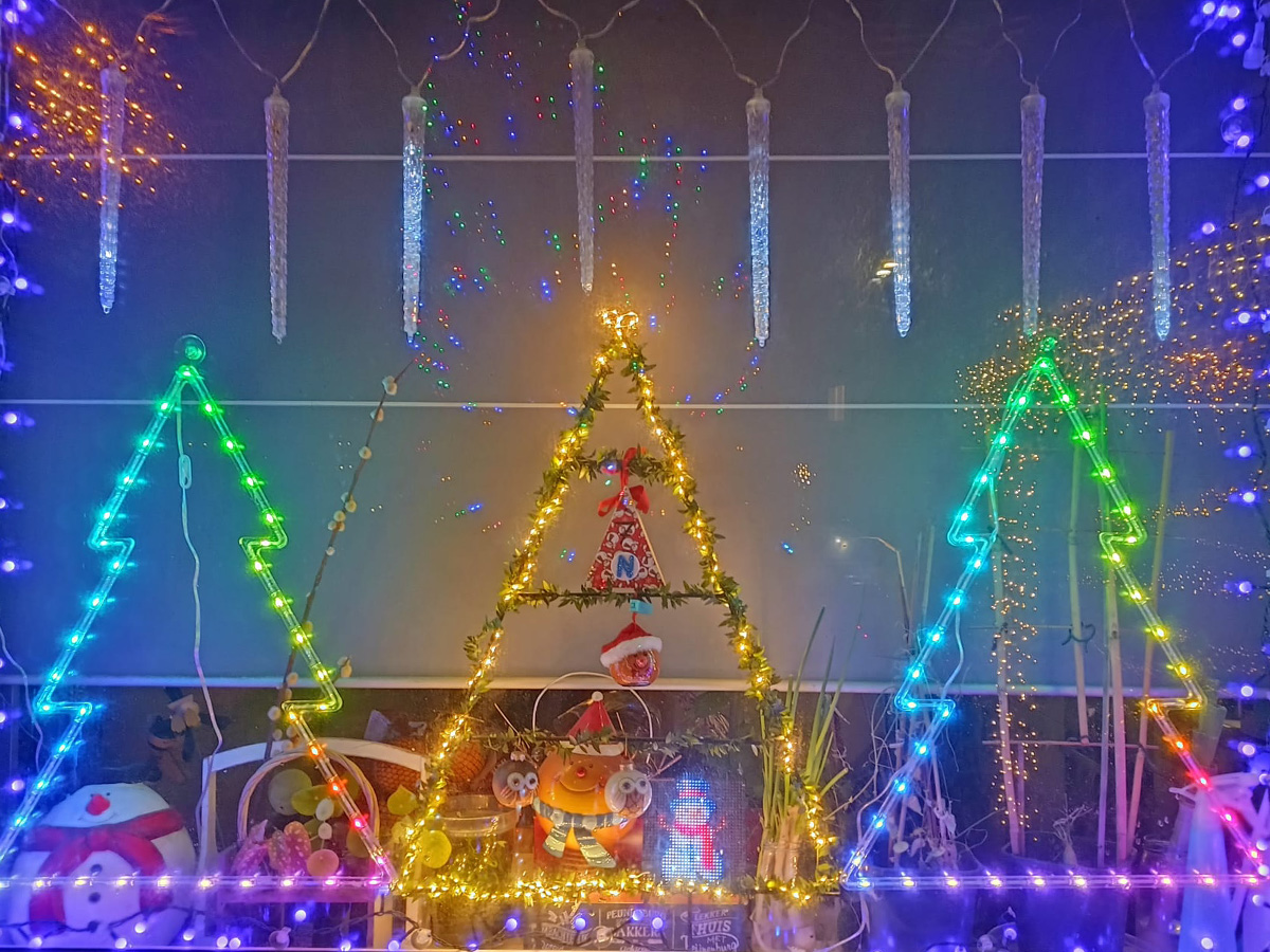 kerstcreatie van 3 gekleurde, verlichte kerstbomen achter een raam